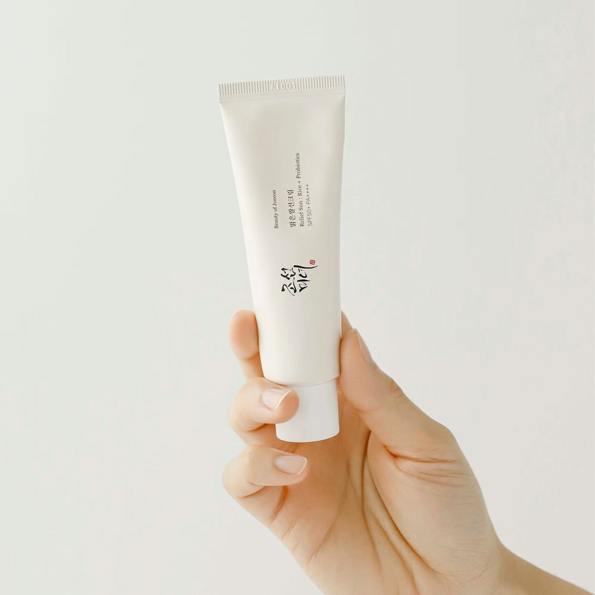 Hand holding the full-size Beauty of Joseon Relief Sun : Rice + Probiotics SPF50+ PA++++ sunscreen tube against a plain background