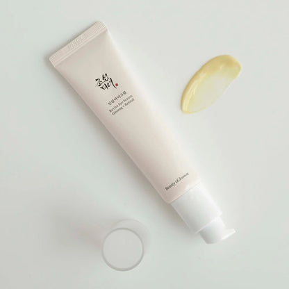 Beauty of Joseon Revive Eye Serum tube lying open with its cap beside a swatch of pale yellow serum texture
