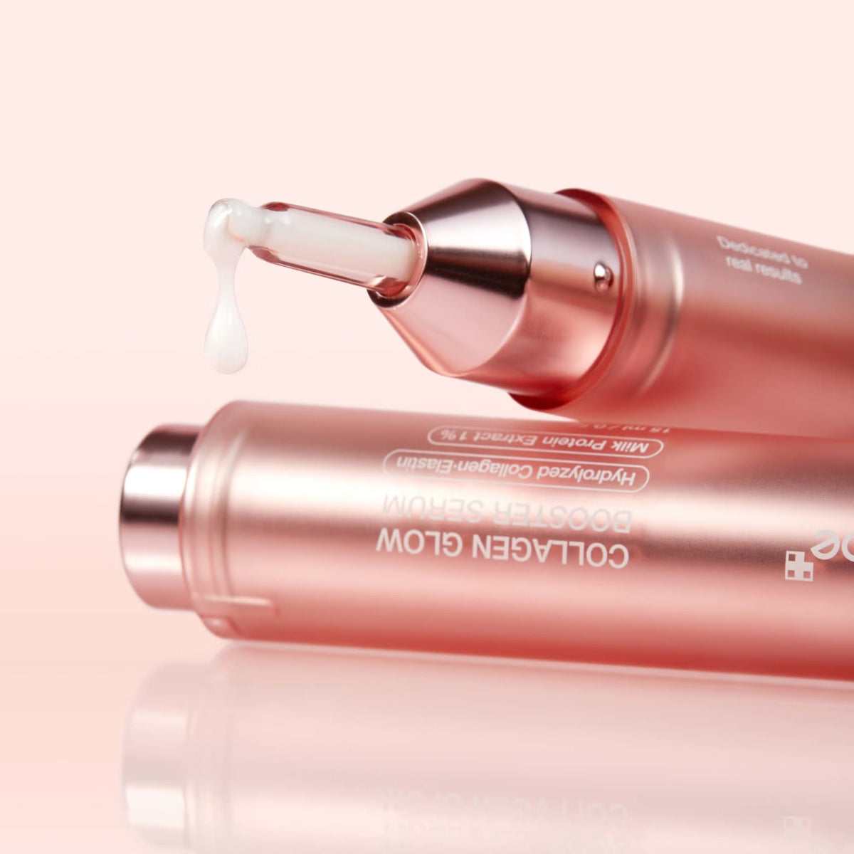 Two medicube Collagen Glow Booster Serum pens with a drop of white milky serum falling from the nozzle, showing the product texture